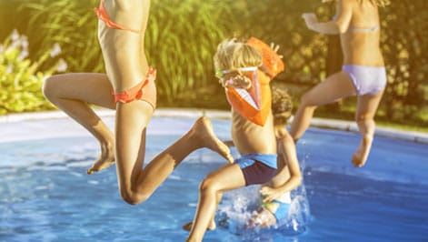 Kids jumping into a clear swimming pool with floaties, having fun and playing together.
