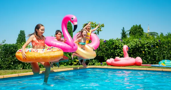 Four children wearing floaties jumping into a crystal clear pool, smiling and having fun.