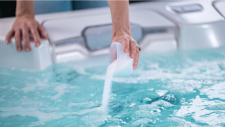 Material being poured from a TruDose™ cap into a hot tub — generic step for adding hot tub supporting chemicals.
