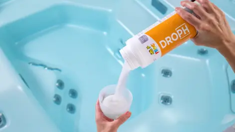 FROG® DropH® being poured into a TruDose™ cap over a hot tub — always adjust total alkalinity first using FROG® Target or DropH® before correcting pH.