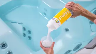 FROG® STOMPS® Non-Chlorine Oxidizing Shock being poured into a TruDose™ cap above a hot tub — helps maintain clear, fresh spa water.